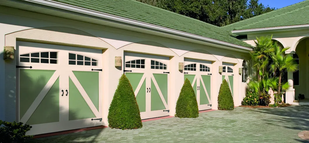 Amarr By Design cream carriage doors on a three car garage with a green roof