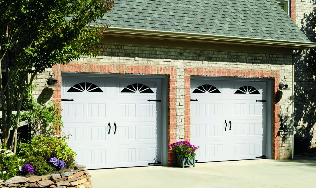 Two white carriage house doors with arched window sections on a stone home