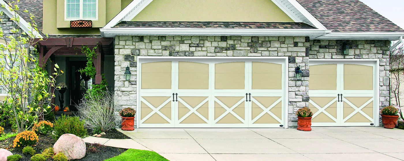 Cream carriage house garage doors with decorative strap hardware on a landscaped drive