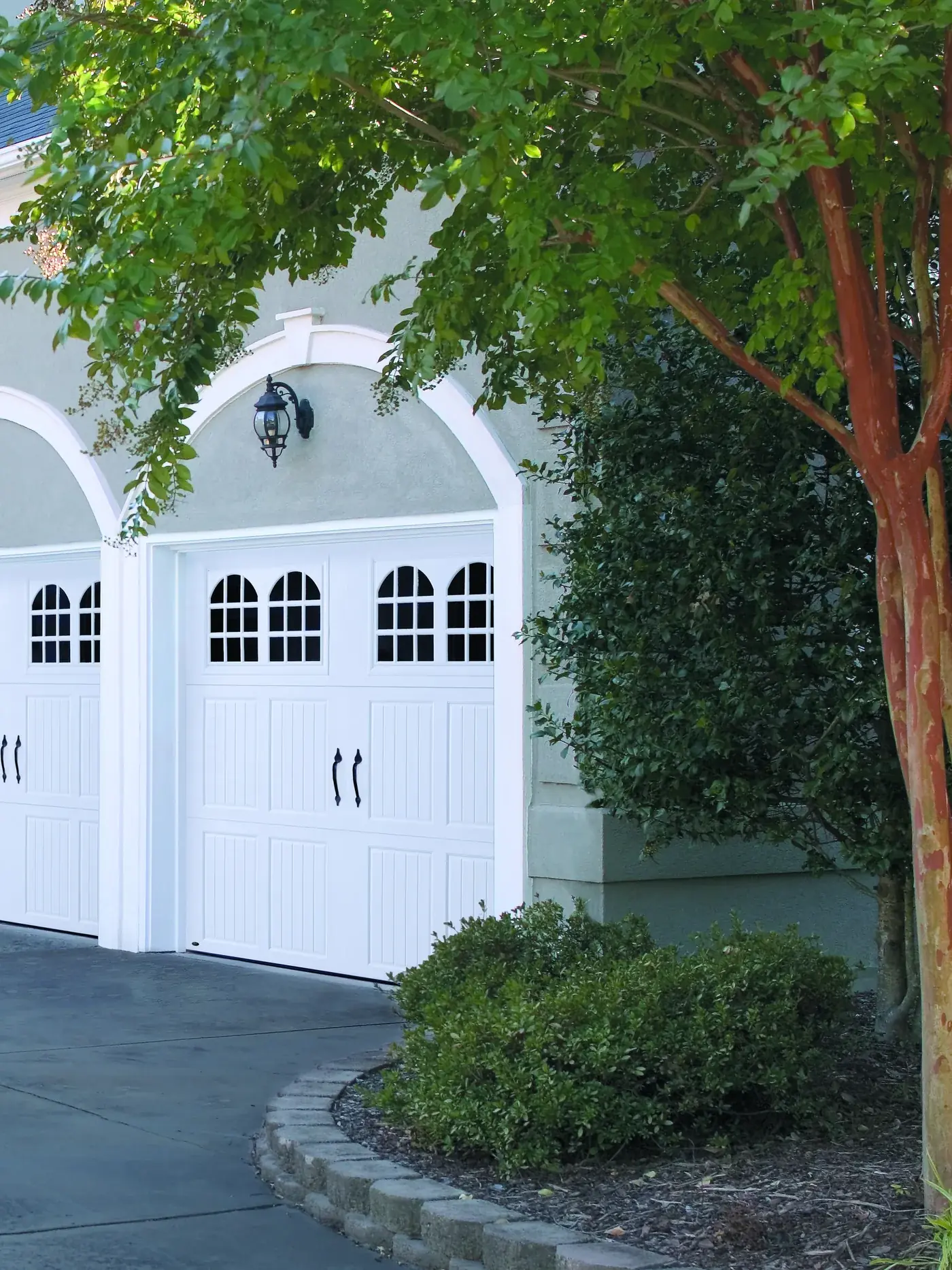 A white estate home with arched carriage house garage doors and mature trees