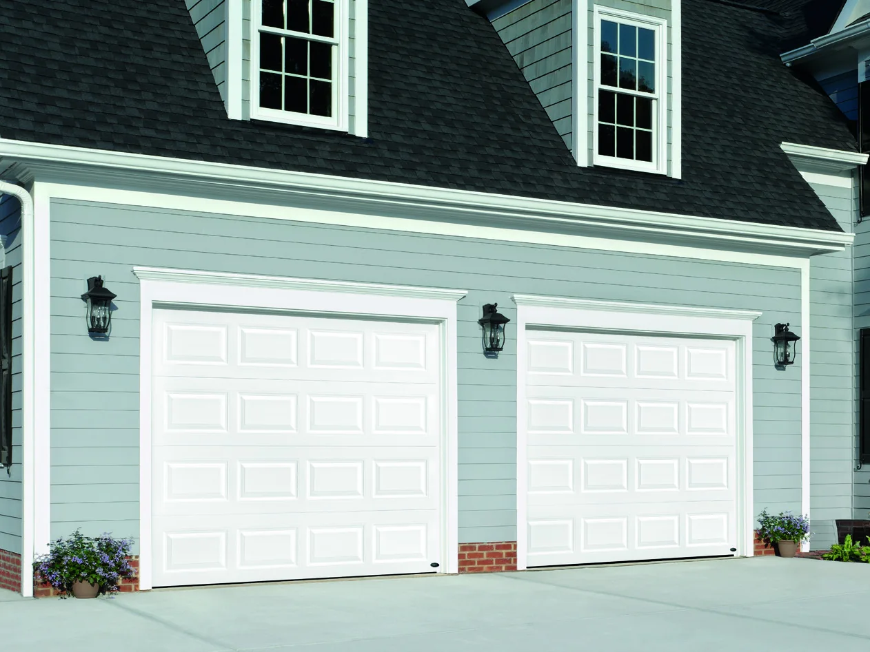 White garage doors on a pale blue coastal home with dormer windows