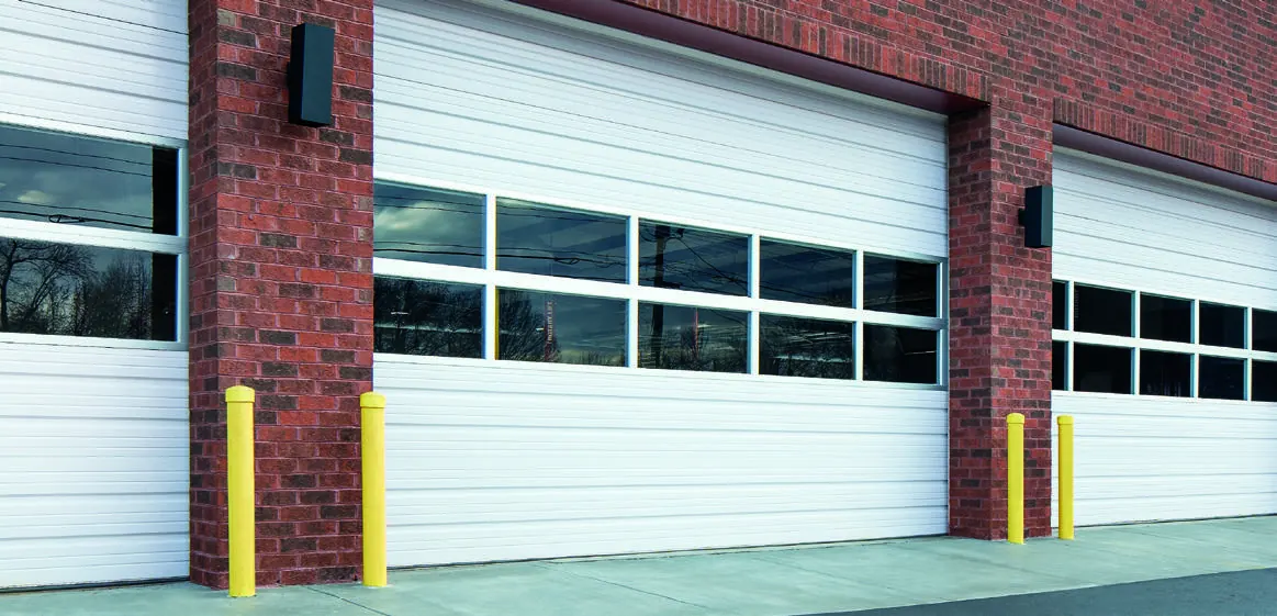 White Amarr 2002 series ribbed steel commercial doors with window rows on a red brick building