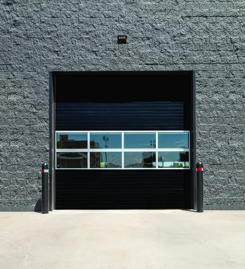 Black Amarr 2432 series commercial door with a full view glass section on a block building