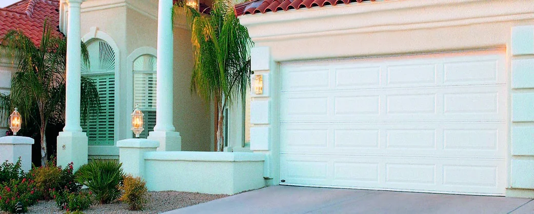 A mint green stucco South Florida home with a white double garage door and palms
