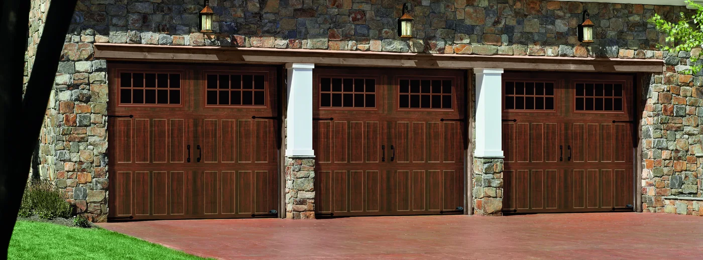 Three woodgrain garage doors on a stone faced three bay garage
