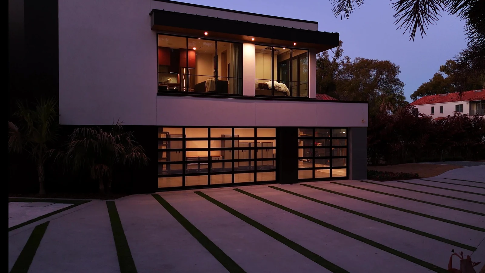 Contemporary Florida home at dusk with palms, warm light behind full view glass garage doors