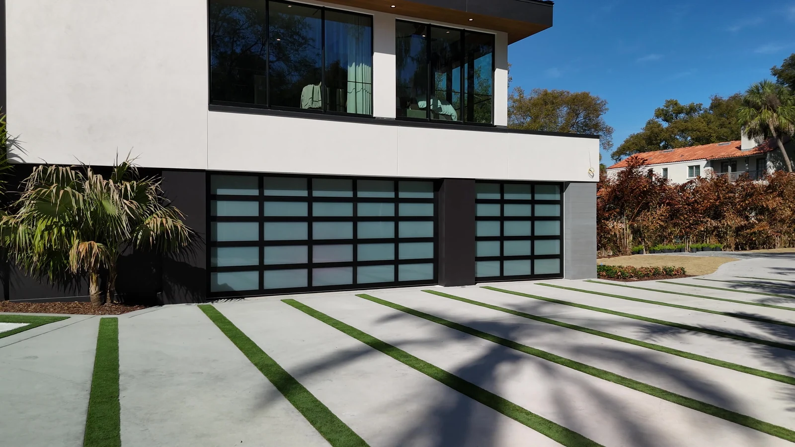 Contemporary Florida home with full view glass garage doors under a first floor overhang, palms either side