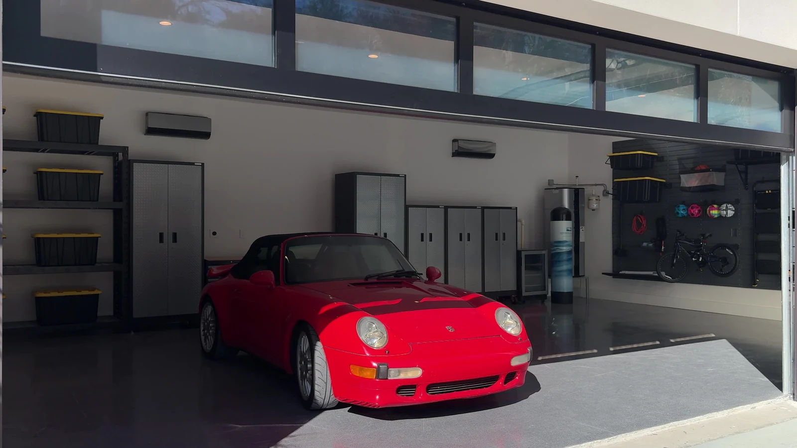 Inside a finished garage lit through a full view glass door, with a sports car parked on polished concrete