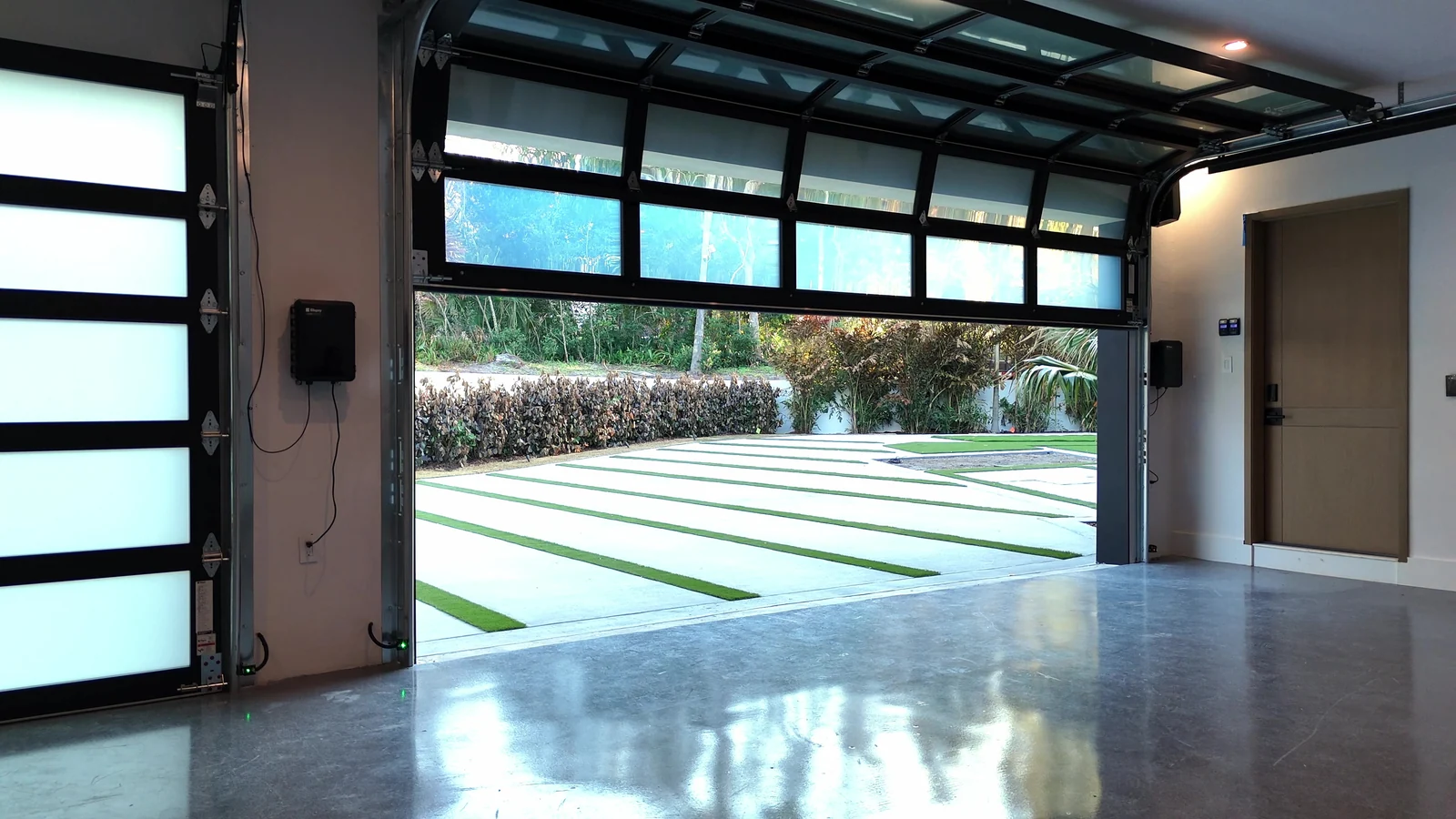 Open full view glass garage door seen from inside, looking out onto clipped hedges and palms