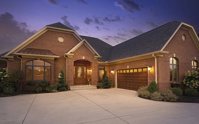 Garage doors lit at dusk on a brick home with a wide paved drive
