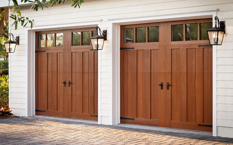 A pair of faux wood carriage doors with white trim and coach lanterns