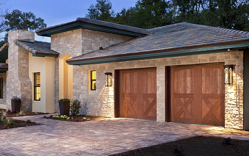 Clopay Canyon Ridge faux wood doors on a stucco home with a tile roof at dusk