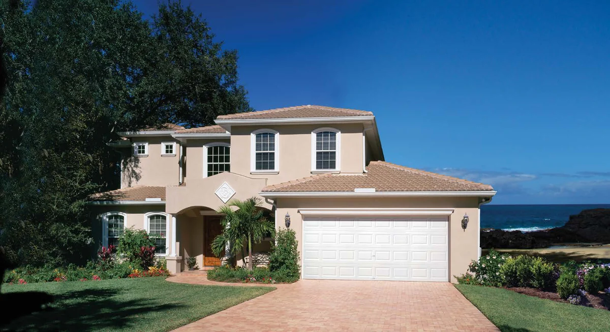 White Clopay raised panel garage door on a stucco Florida home with a tile roof and the ocean behind