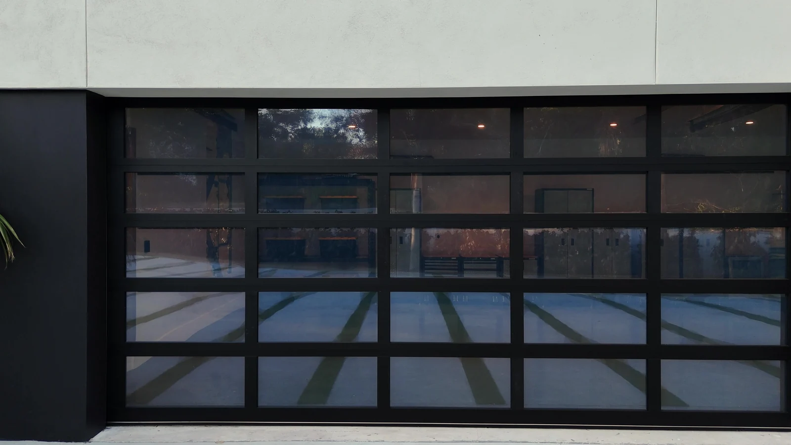 Wide black framed full view glass garage door across a modern stucco elevation
