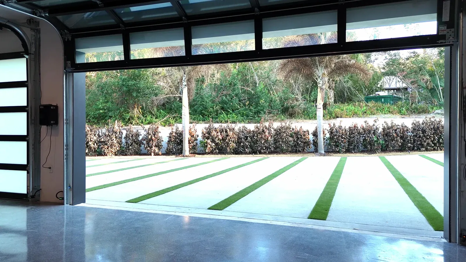 Open full view glass door looking out onto clipped hedges and a grass strip drive
