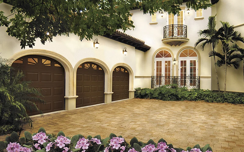 Arched Clopay carriage doors on a Mediterranean style home with a paver drive