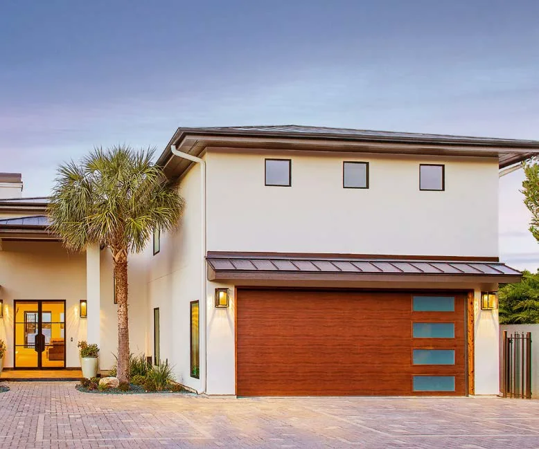 A modern South Florida home at dusk with a wood grain garage door and a palm in the courtyard