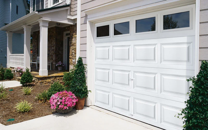 White raised panel garage door with window inserts on a brick home
