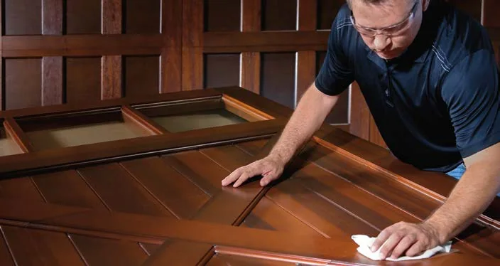 Hand applying finish to a mahogany garage door section