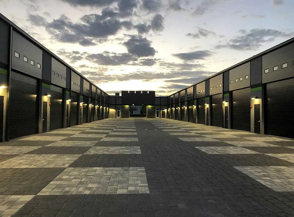 Amarr 2432 full view commercial door, row of Amarr 2432 insulated steel doors in Black along a garage condo lane at dusk