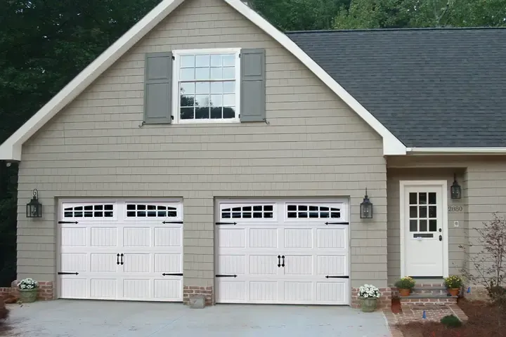 Raynor Aspen AP138 garage door, two white carriage style doors with windows on a grey sided home