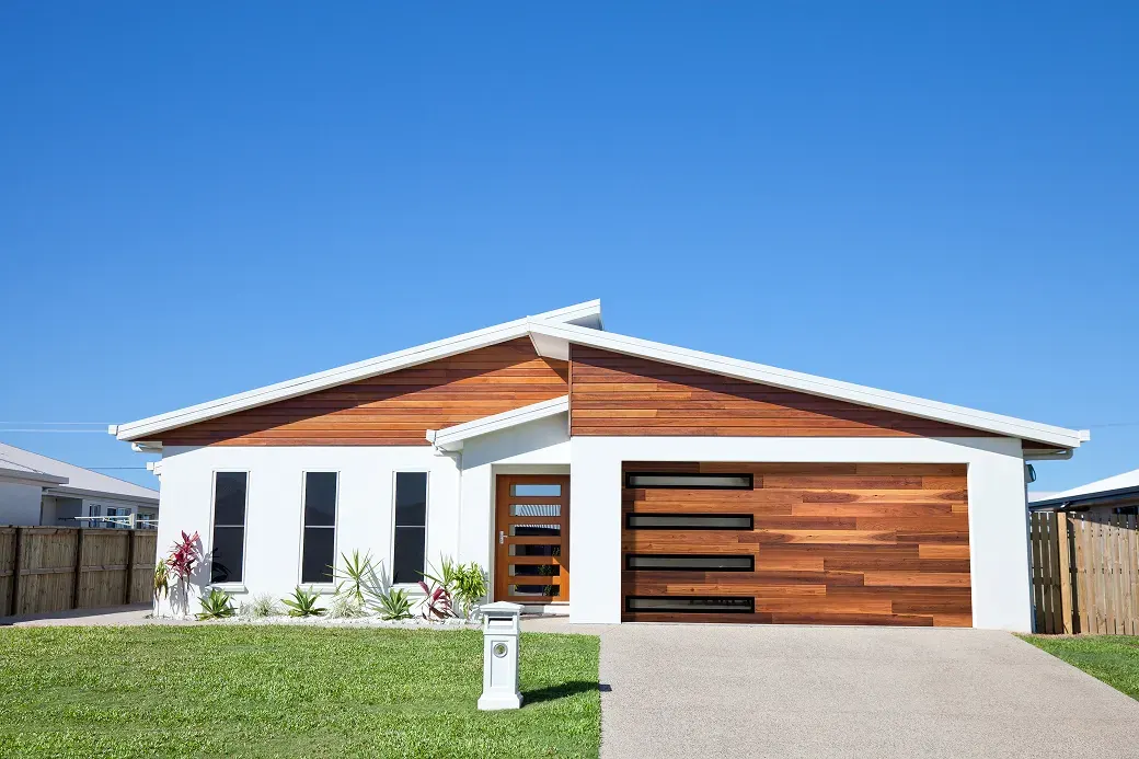 Puerta de garaje Raynor Aspen Contempra, puerta de tablón en tono madera con ventanas delgadas en una casa moderna blanca