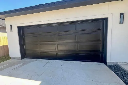 Puerta de garaje Raynor BuildMark, puerta doble negra de paneles realzados en un garaje blanco