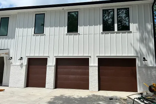 Puerta de garaje Raynor Encore, tres puertas cafés lisas en una casa blanca de tablas verticales