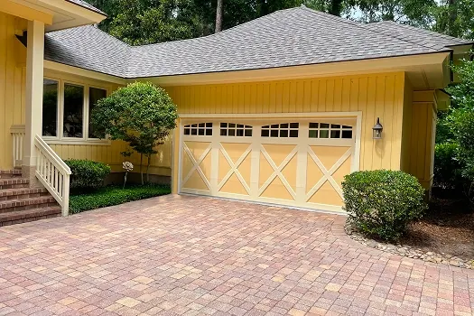 Puerta de garaje Raynor RockCreeke, puerta color arena con cruz en X en una casa amarilla