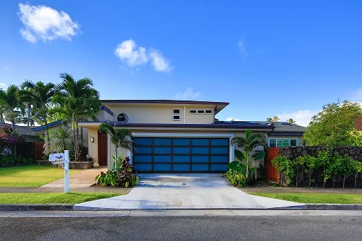 Puerta de garaje Raynor StyleView, puerta con marco negro y vidrio azul en una casa moderna de Florida con palmas