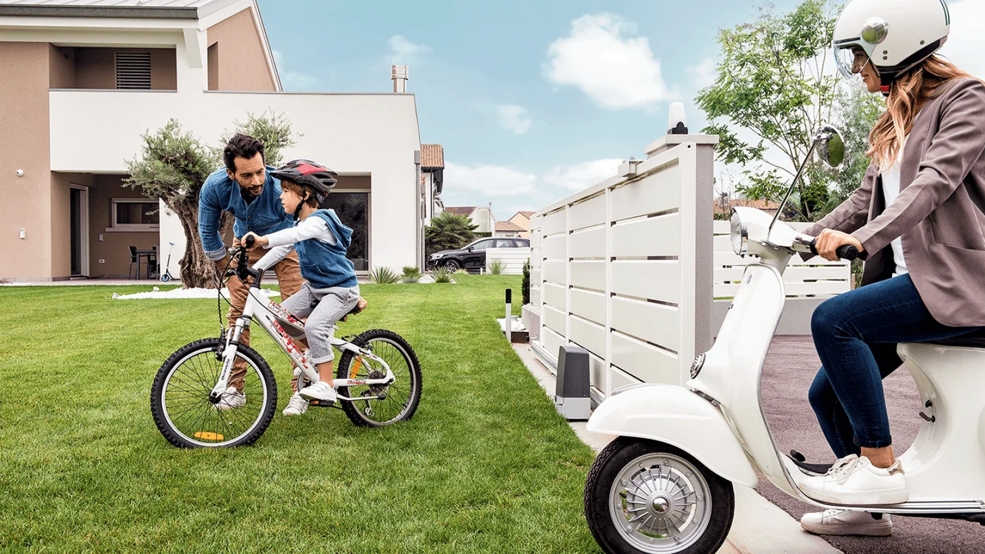 A family in the yard behind a closed automatic driveway gate