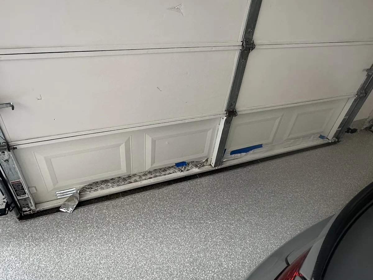 A garage door bottom section part way through replacement, the new panel set against the opening