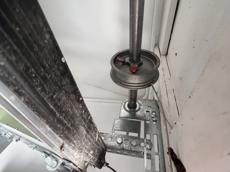 A cable drum and end bearing plate on the torsion shaft at the side of a garage door, with a wrench on the hardware