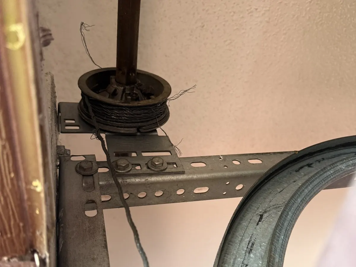 Lift cable wound onto the drum at the end of the torsion shaft above a garage door, with the spring beside it