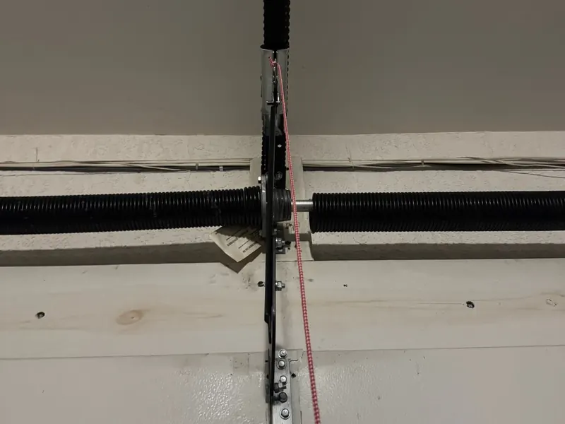 Close-up of a center bearing plate with a torsion spring on each side and the opener release cord hanging down