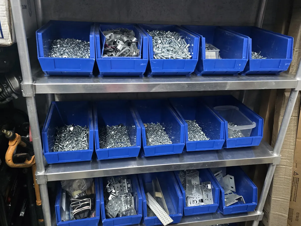 Racked parts bins holding rollers, hinges, brackets and fixings, with a boxed opener rail stored above