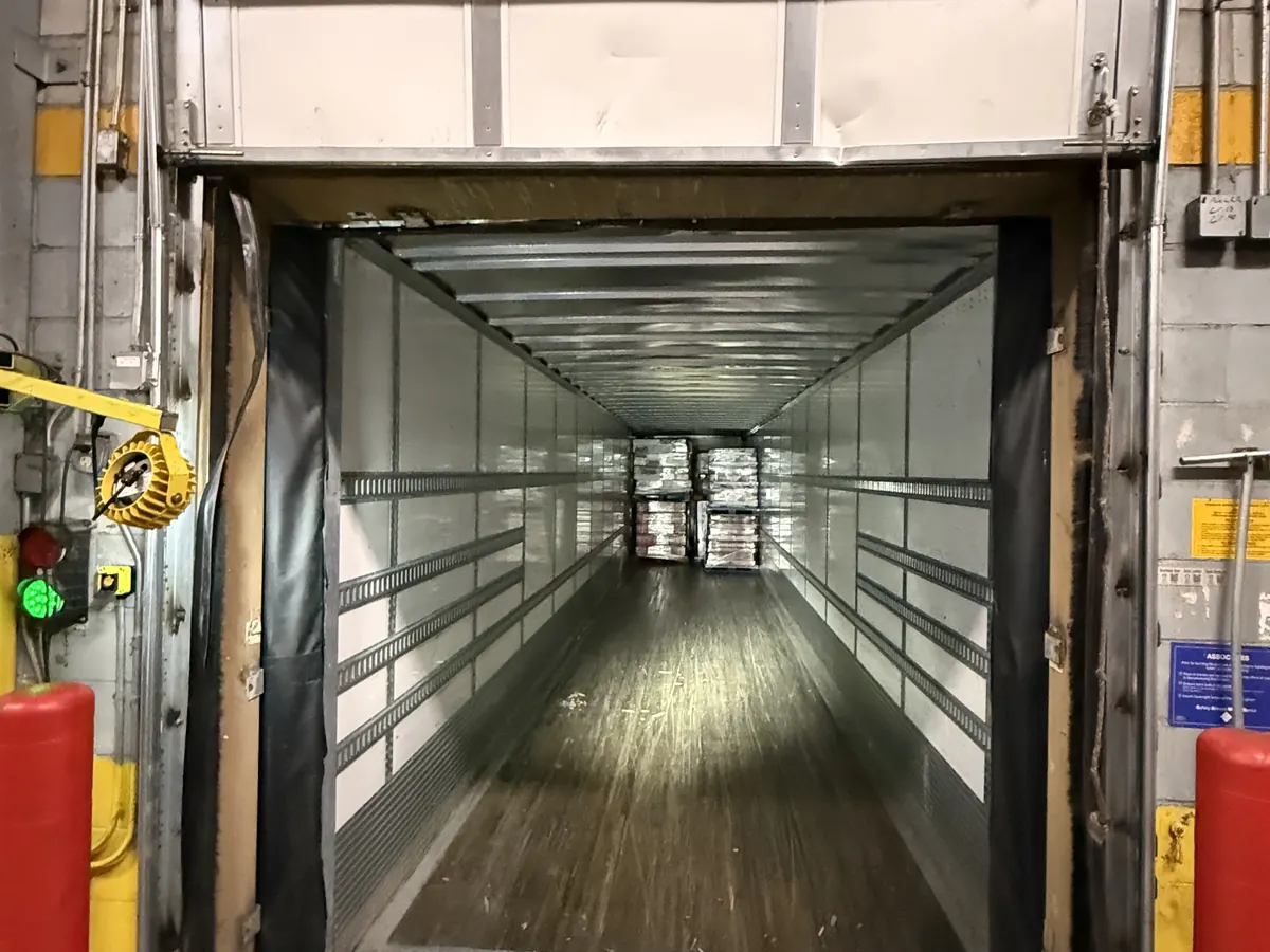 A loading dock door raised with a trailer backed into the dock seal, seen from inside the warehouse