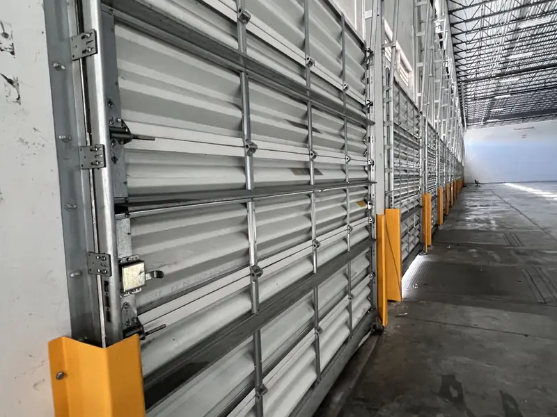 Angled view along a row of commercial sectional doors inside a warehouse, with galvanized tracks and orange guard posts at the openings