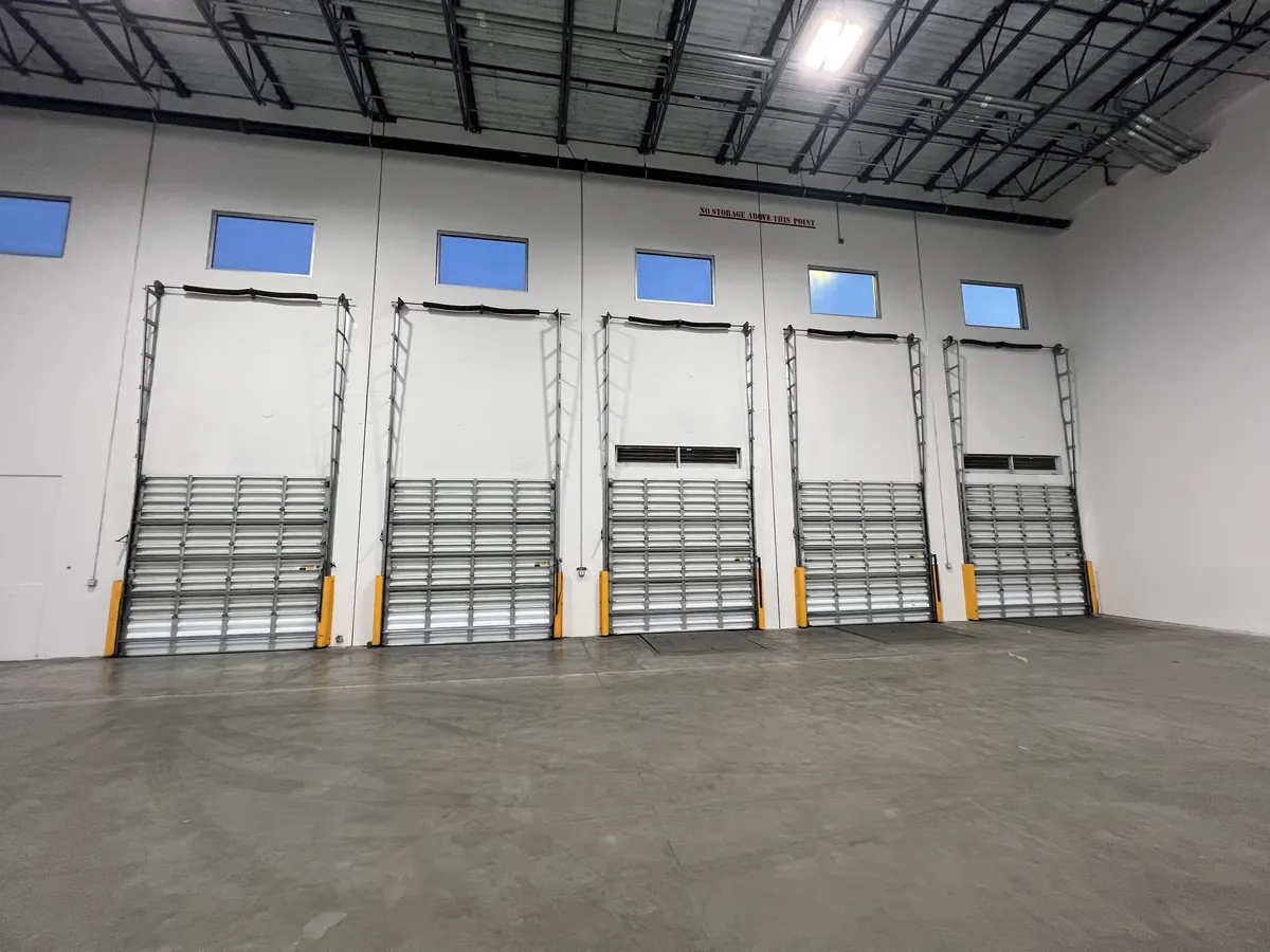 Five loading bay openings side by side in a finished warehouse, each with an insulated door above a folding steel security gate