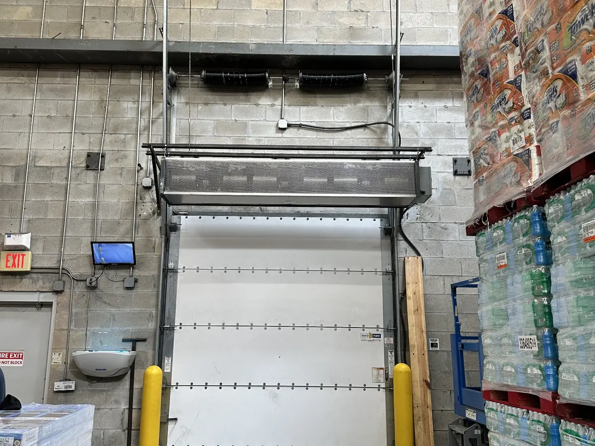 A white insulated sectional door in a retail stockroom with a jackshaft operator mounted beside the opening