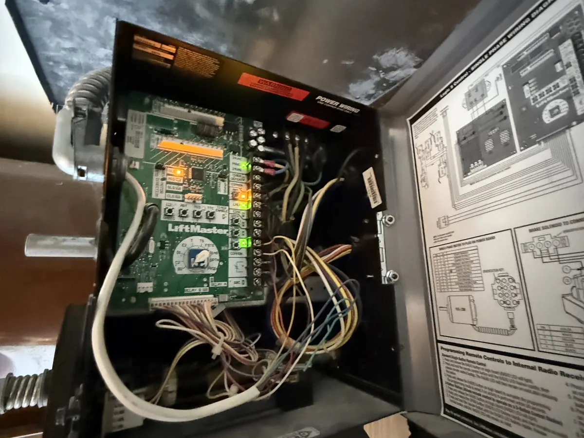 The open control panel of a LiftMaster commercial door operator, showing the logic board and field wiring against the wiring diagram inside the cover
