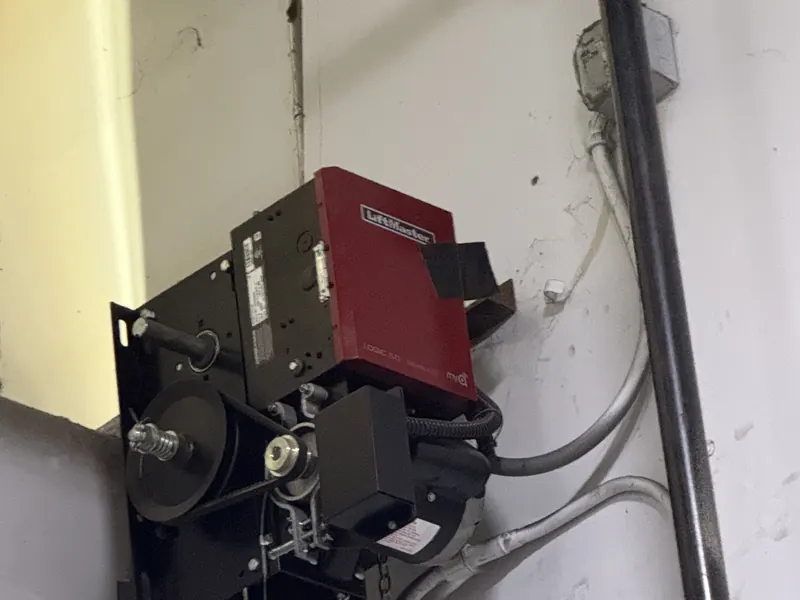A commercial garage door operator with a red LiftMaster control box mounted on a wall, with the drive chains and conduit running to it