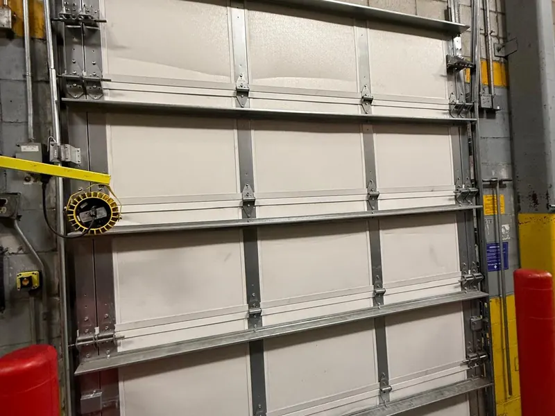Interior view of a white insulated sectional commercial door with reinforcing struts and vertical tracks in a loading bay
