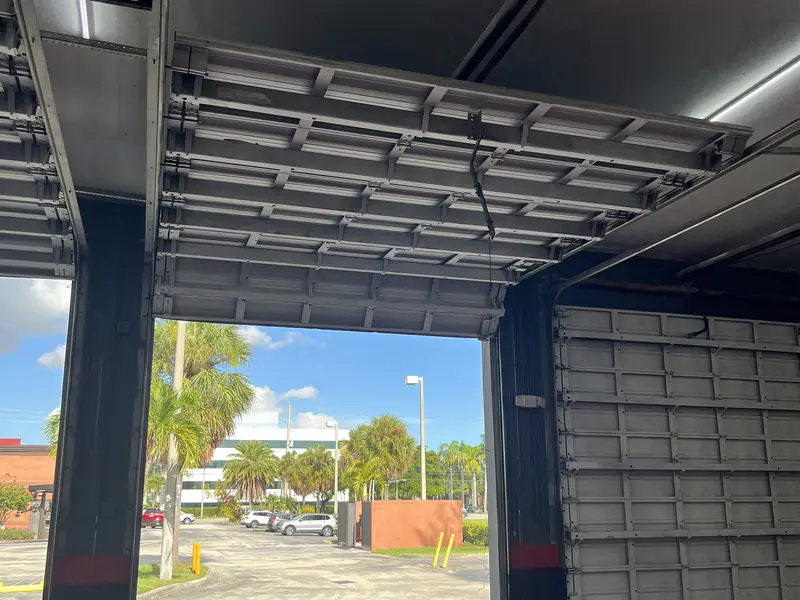An open commercial sectional door with its panels retracted overhead and an operator mounted beside the opening