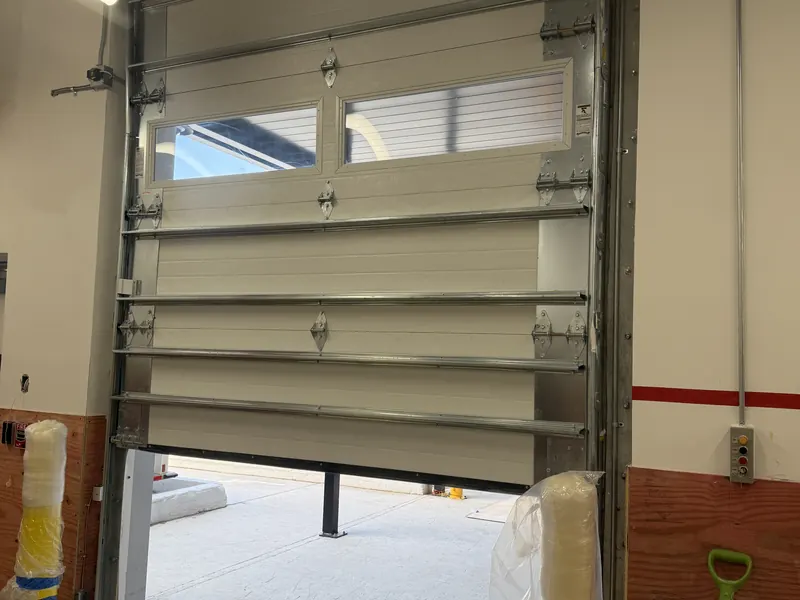 Commercial sectional door raised part way inside a service bay, showing the vision panels, struts and vertical tracks