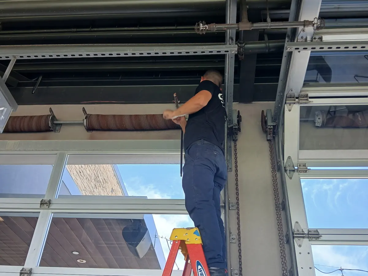 A technician on a ladder setting the top section of a glazed commercial sectional door into its track