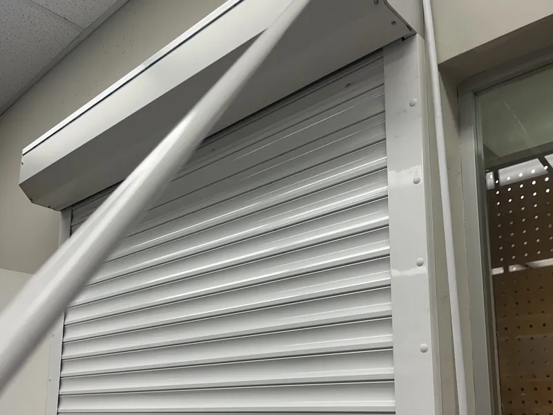 White coiling counter shutter closed over an interior service window, with its hood and side guides fitted