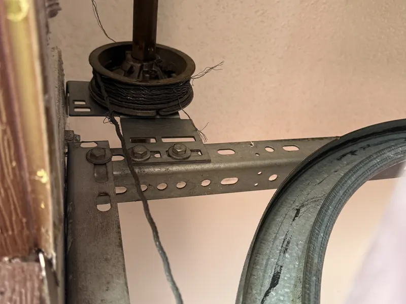 Frayed lift cable wound on a cable drum at the top corner of a garage door track