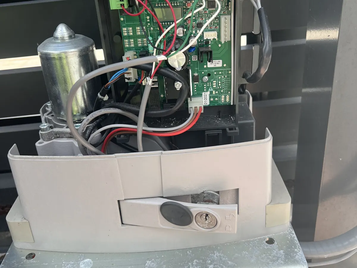 Slide gate operator opened at the control board, capacitor and limit switch adjustment plate visible inside the housing