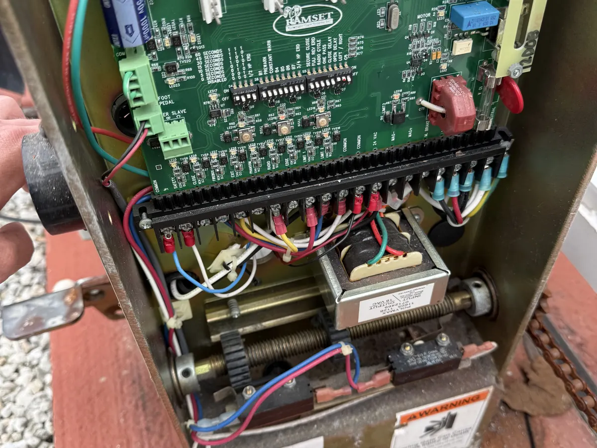 Gate operator cabinet opened for service, showing the motor, the drive springs and the wiring landed on the terminal board